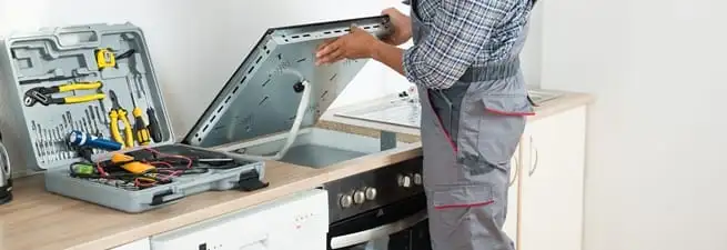 Cooktop repair technician lifting a built-in stovetop for service in Newark, NJ