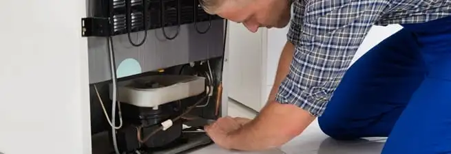 Refrigerator repair technician servicing the compressor and condenser area in Newark, NJ