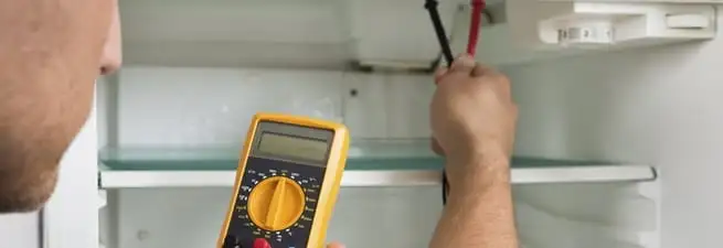 Refrigerator repair technician testing electrical components with a multimeter in Newark, NJ